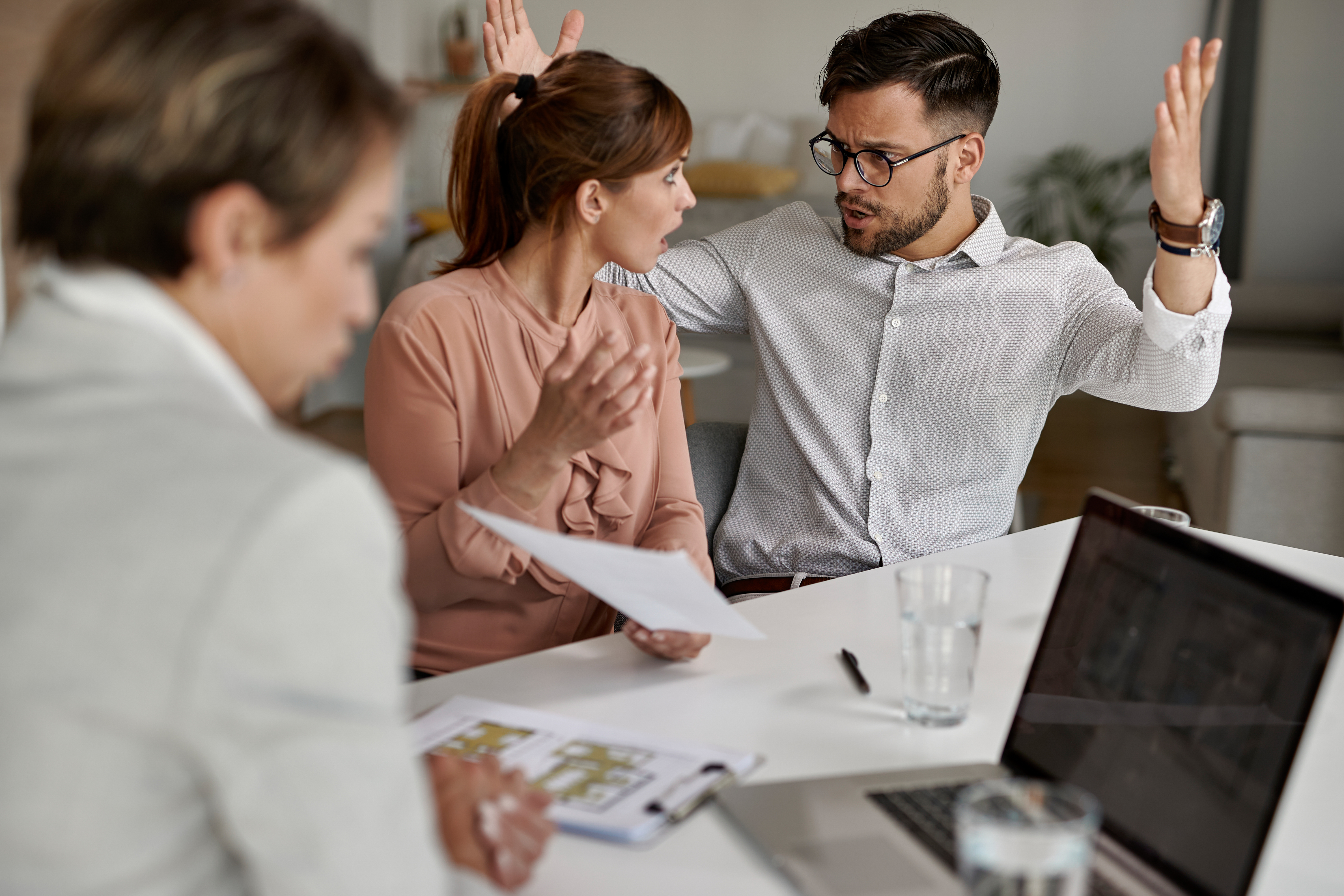 Young displeased couple arguing while having a meeting with real estate agent.